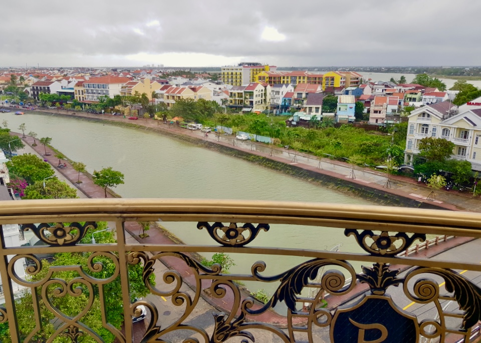 A gold painted ornate railing overlooks a green river and colorful houses.