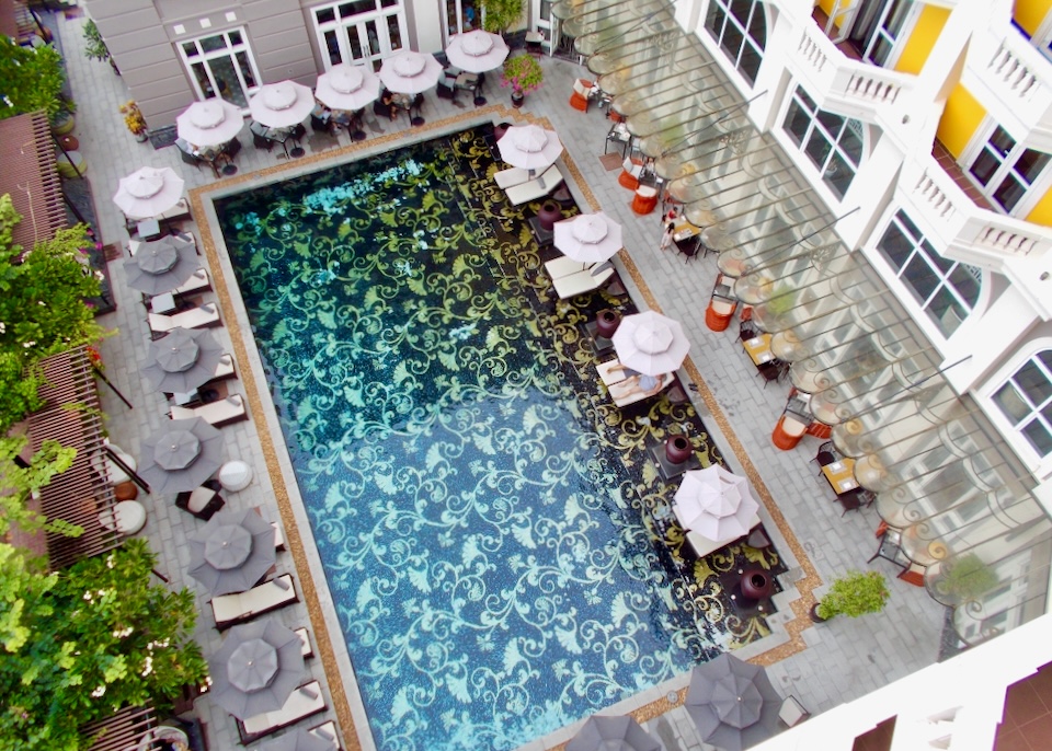 View looking down from a top floor at a pool with a floral pattern and lounge chairs.