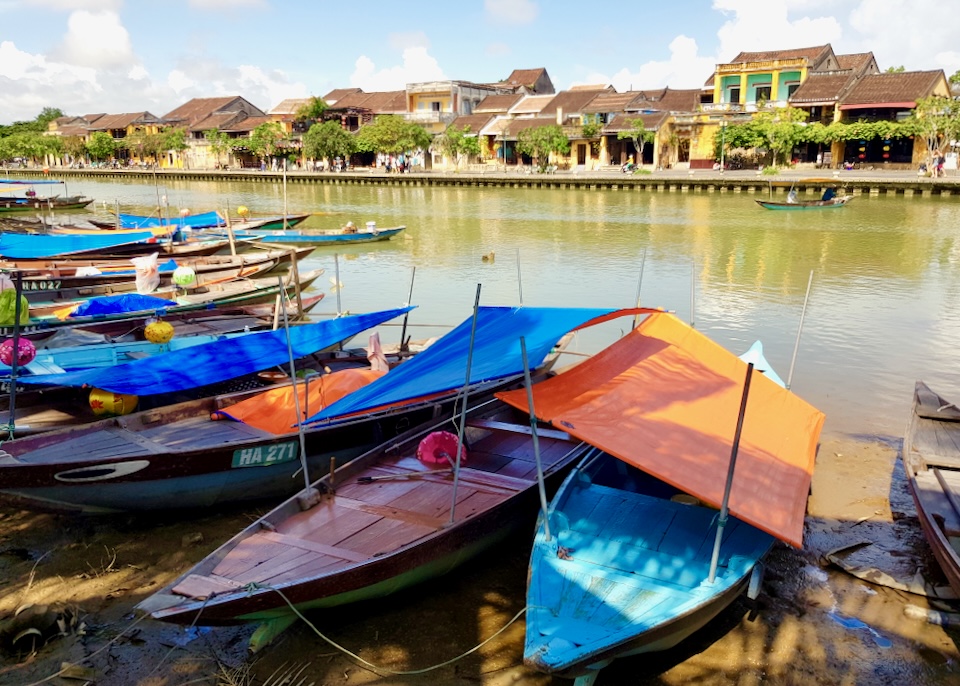 Colorful small wooden boats sit on a clay shore next to a green river.