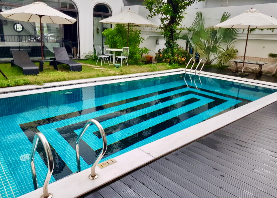 A blue pool with dark sits next to green grass and brown lounge chairs.