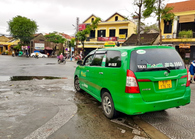 A bright green taxi van drives on a street outside the Old Town.