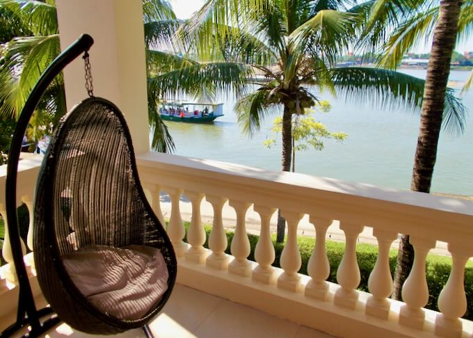 A chair on a swing sits on a balcony next to a river.