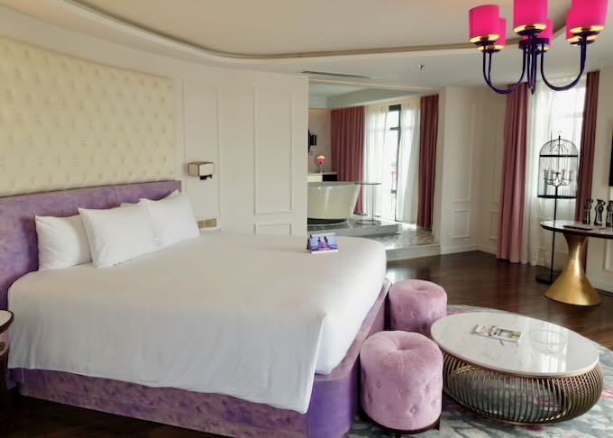 A plush purple bed in a large hotel room.