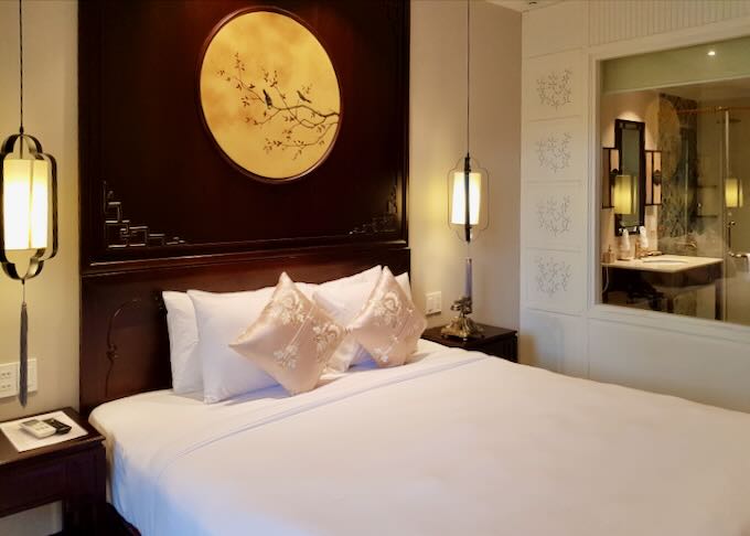 A white bed with silk pillows and a dark wood headboard with a gold circle.