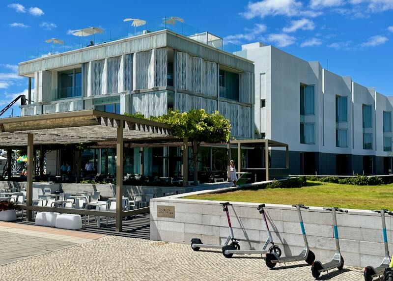 Modern hotel with a covered terrace, green lawn, and scooters parked in front