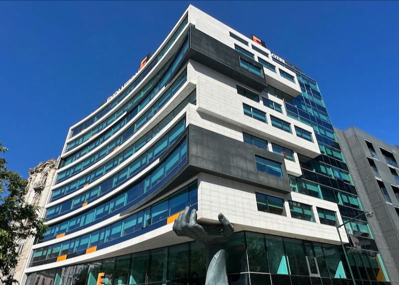 Exterior of a modern hotel, looking like it's being hoisted at one corner by a giant hand