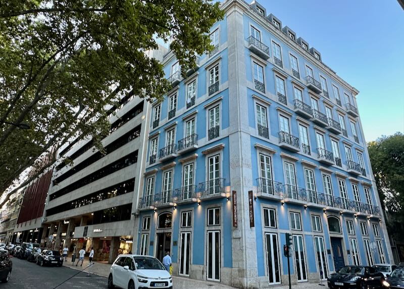 Corner view of a pastel blue hotel with white trim and wrought-iron juliet balconies in Lisbon