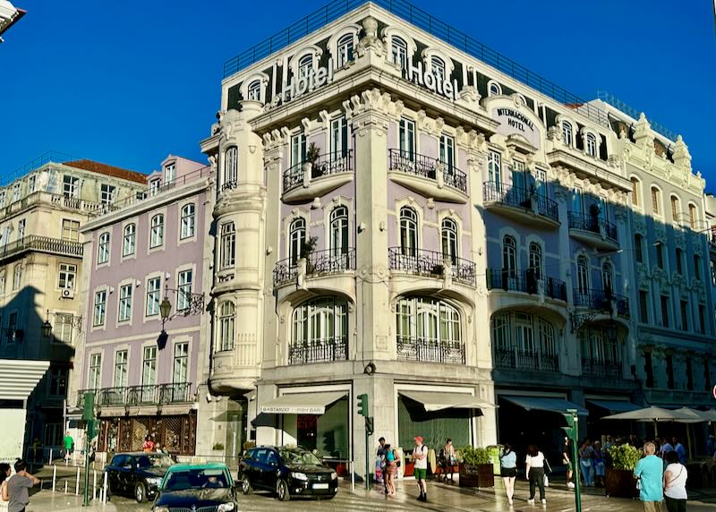 Ornate lilac-colored hotel at the corner of a busy street in Lisbon