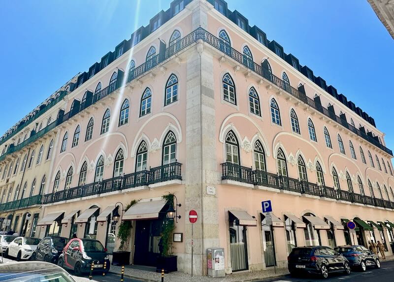 Corner view of a pink historic hotel in Lisbon with arched windows and white trim