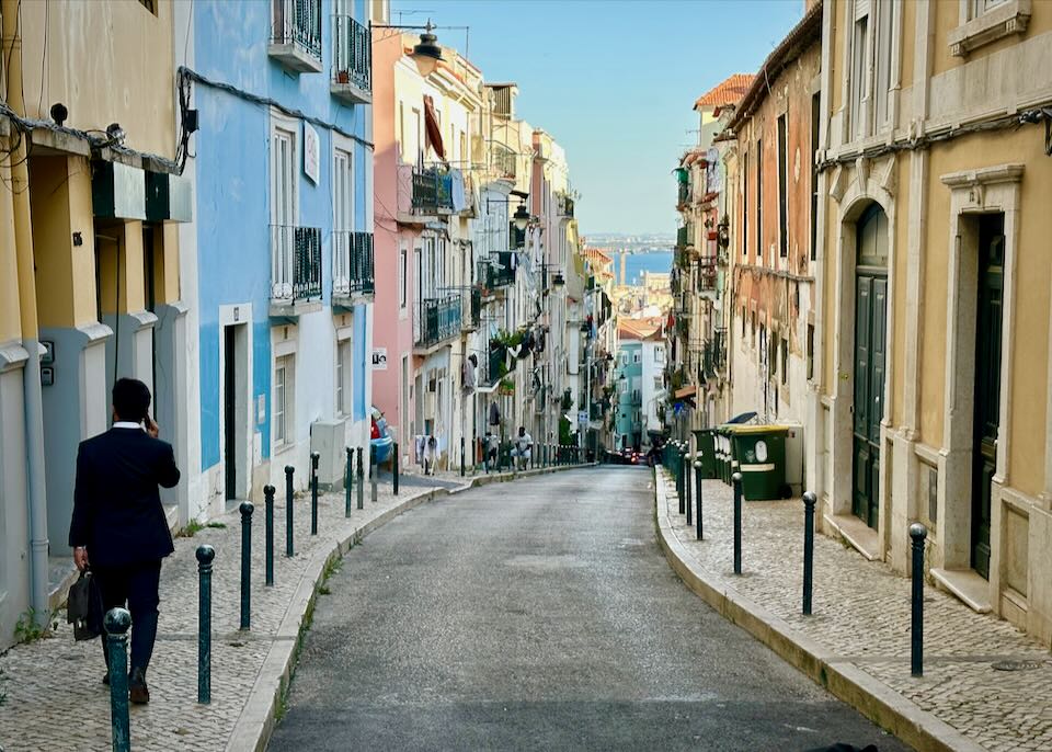 A man walks down a narrow street lined with colorful buildings in Lisbon.