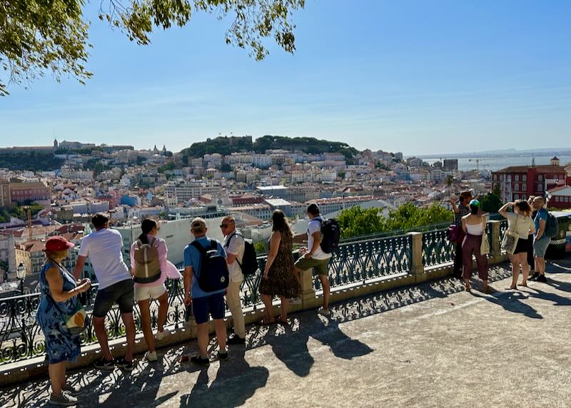 People look out over the rooftops of Lisbon from a pedestrian overlook. 