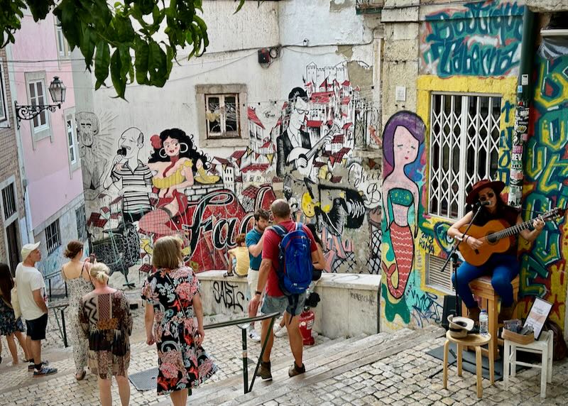A woman sings and plays guitar in a grafitti-laden stairway for passersby.