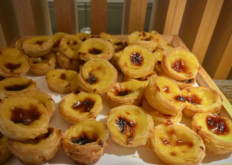 A pile of golden brown pasteis de nata on a paper-lined basket