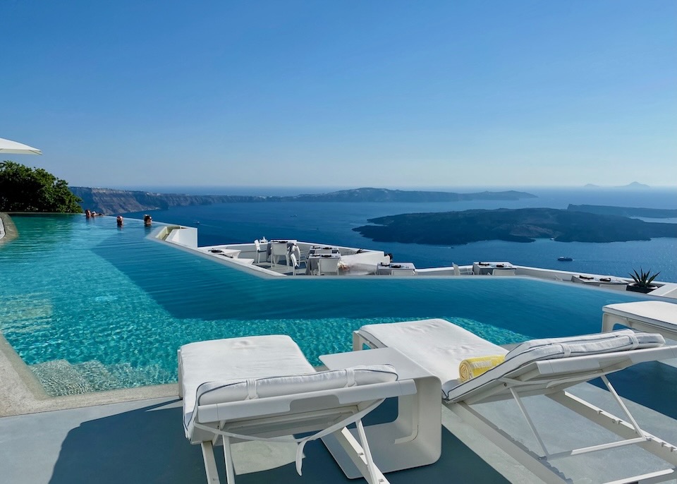 An infinity pool and restaurant overlook the caldera, sea, and volcano in Santorini, Greece