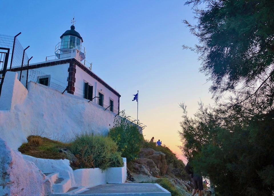 The whitewashed lighthouse in Akrotiri reflecting the colors of the sunset in Santorini