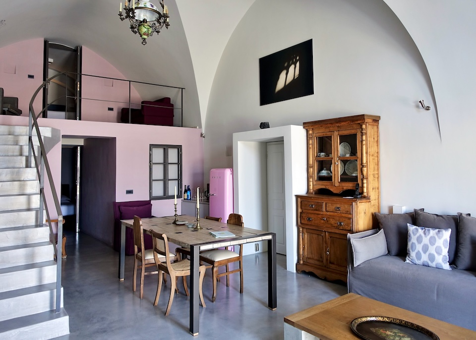 Inside a maisonette suite with a mix of traditional and modern furniture, a stairway leading to the loft, and a vaulted ceiling at a hotel in Santorini