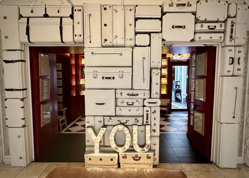 Hotel wall made out of white suitcases, with the word "YOU" lit in a glowing sign.