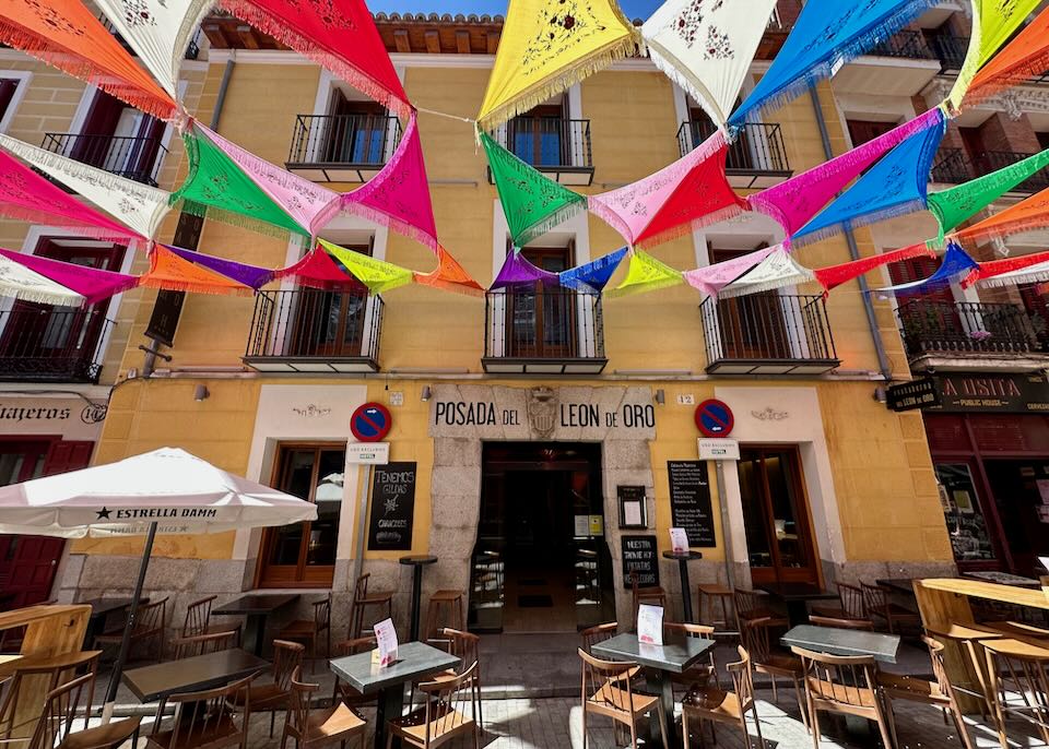 Yellow stucco exterior of a historic hotel in Madrid, with a shaded seating area in front. 