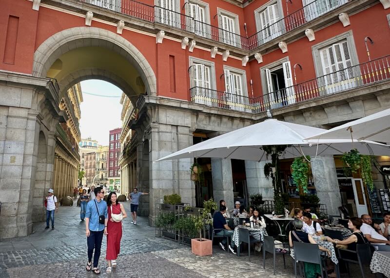 A couple strolls, holding hands, under an archway in Plaza Mayor, Madrid