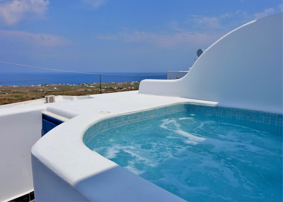 An outdoor jacuzzi painted white on the outside with blue tiles inside and a view to the eastern side of the island and sea at Anemomilos hotel in Oia, Santorini.