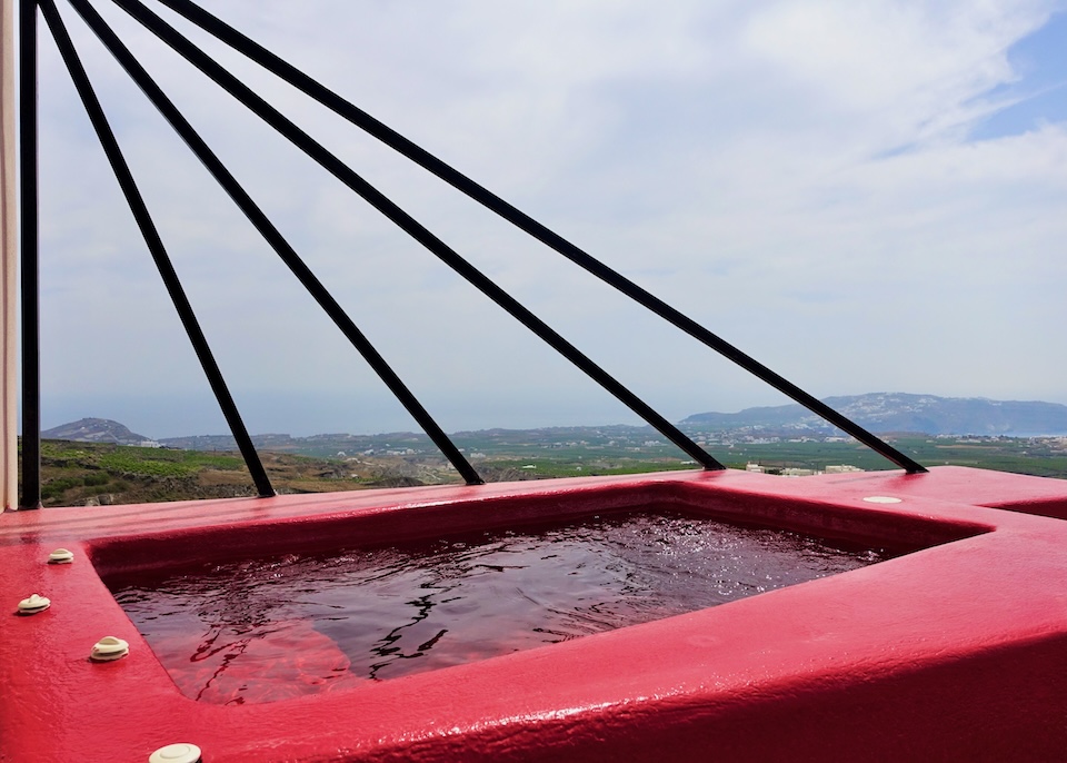 A red painted jacuzzi with black bars arranged like rays on one side and a vineyard view at Art Hotel in Pyrgos, Santorini.