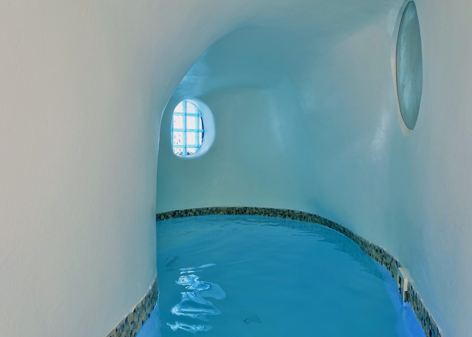 A curved, indoor cave pool with white walls and two round porthole windows at Aspaki hotel in Oia, Santorini.