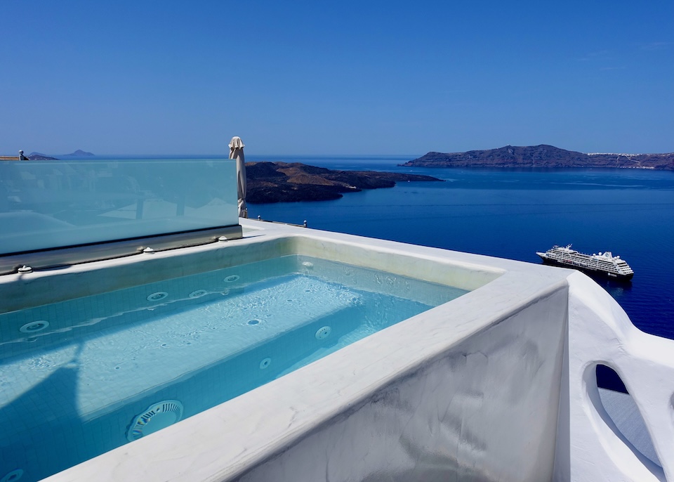 A private jacuzzi above the caldera with views to the volcano and a cruise ship at Athina Luxury Suites in Fira, Santorini