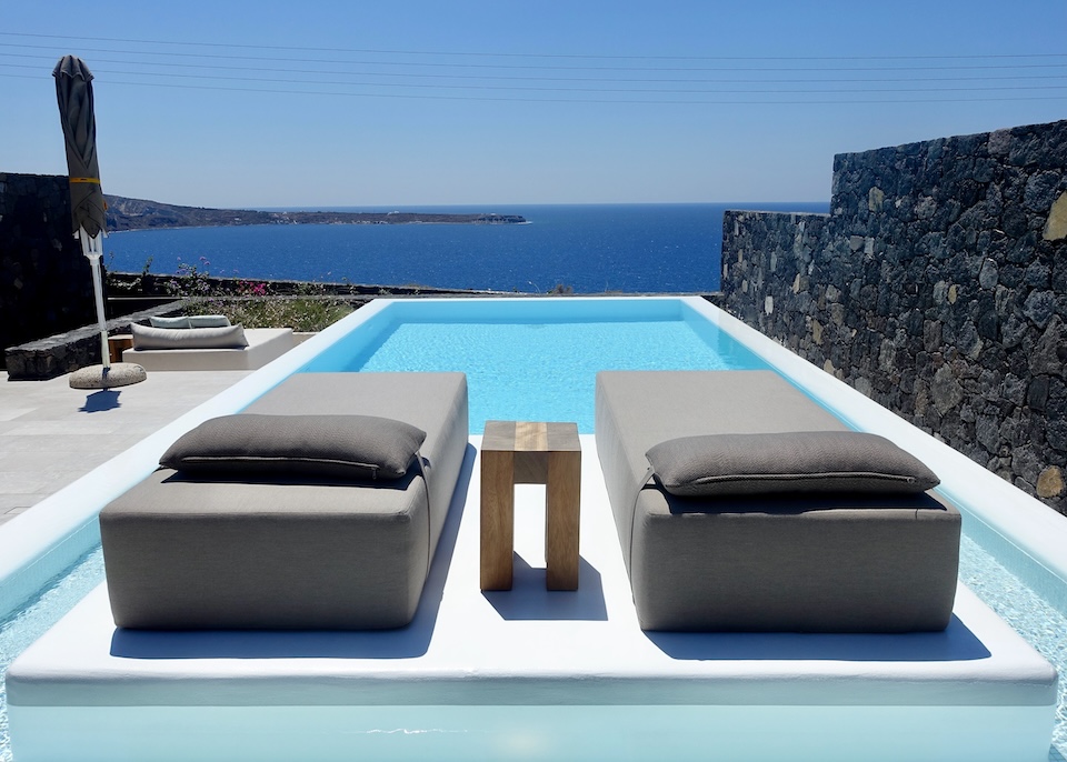 A rectangular private pool with two sunbeds set atop a small island at the near end and a view out to the sea at Canaves Epitome in Oia, Santorini.