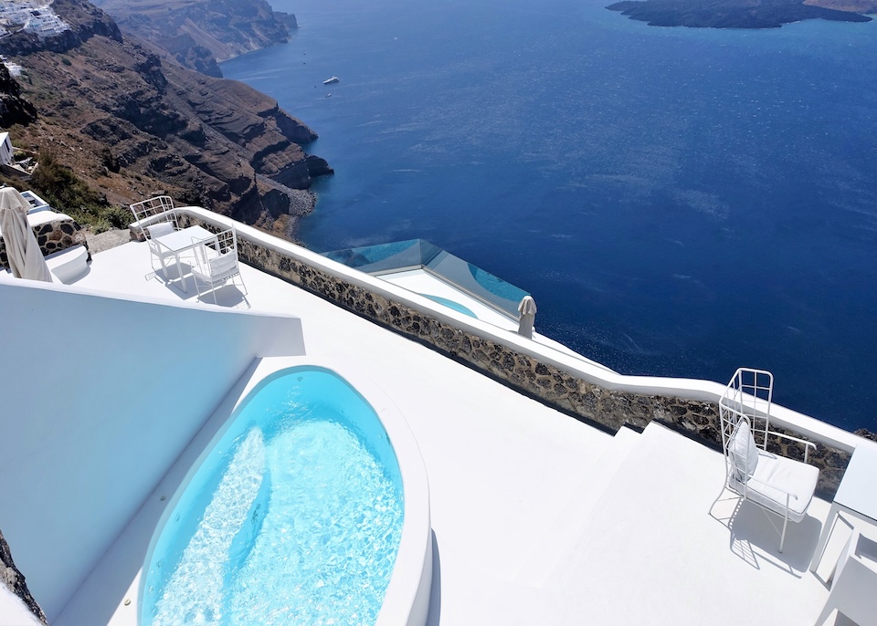 An oval-shaped private jauzzi on a bright white terrace above the caldera with volcano views at Katikies Chromata hotel in Imerovigli, Santorini.