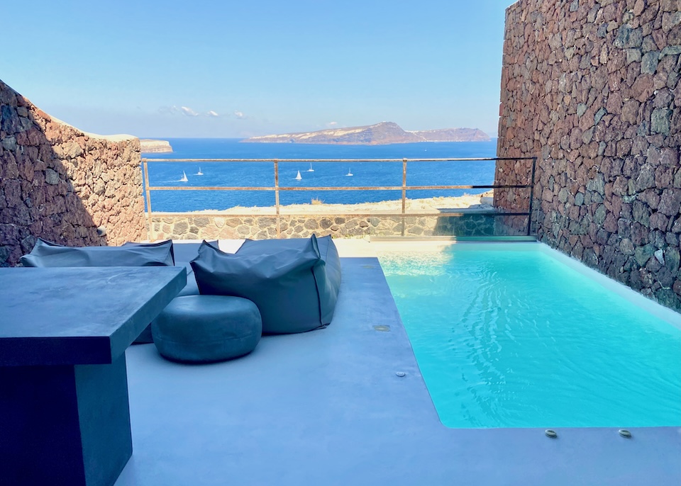 An infinity pool on a furnished terrace with high lava rock walls and facing the caldera at Cocomat hotel in Akrotiri, Santorini.