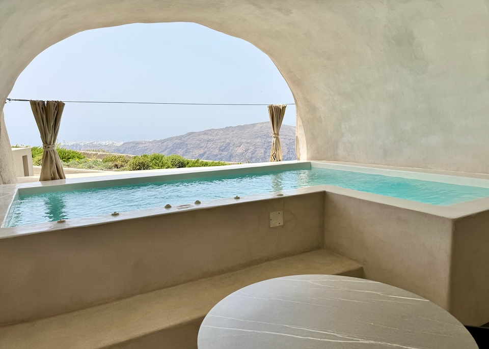 An L-shaped private pool set in a cave with a view toward Oia village in the distance at Divine Cave Experience in Imerovigli, Santorini.