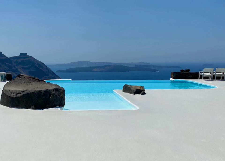 An infinity pool bounded by two boulders above the caldera with Skaros Rock and the volcanoes in the distance at Aenaon Villas in Imerovigli, Santorini