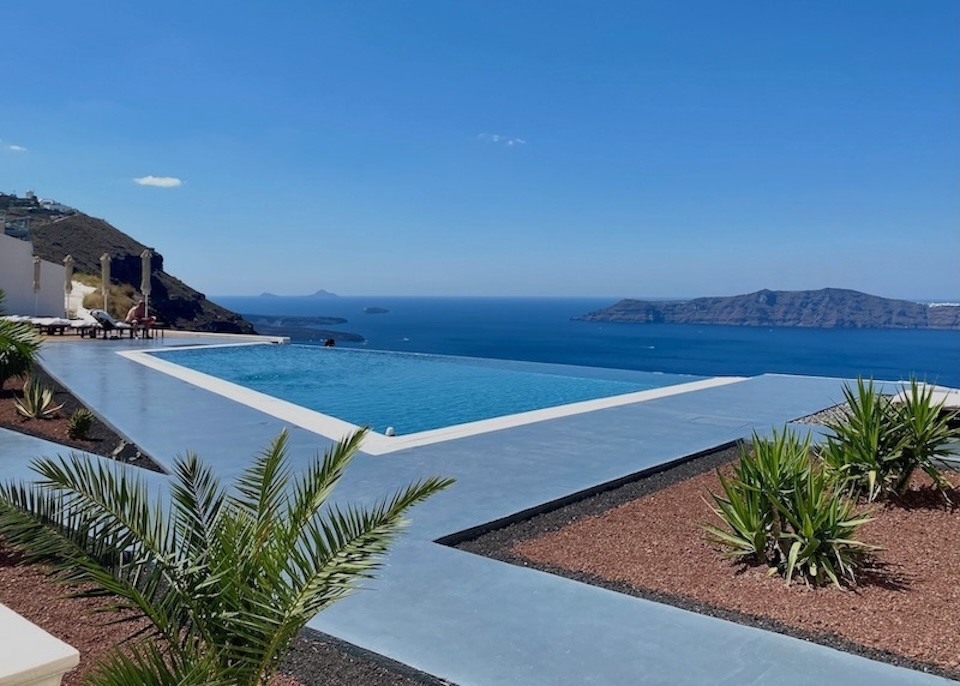 An infinity pool with an edge that appears to blend into the sea perched above the caldera with a view toward Thirassia at Anastasis Apartments in Imerovigli, Santorini.