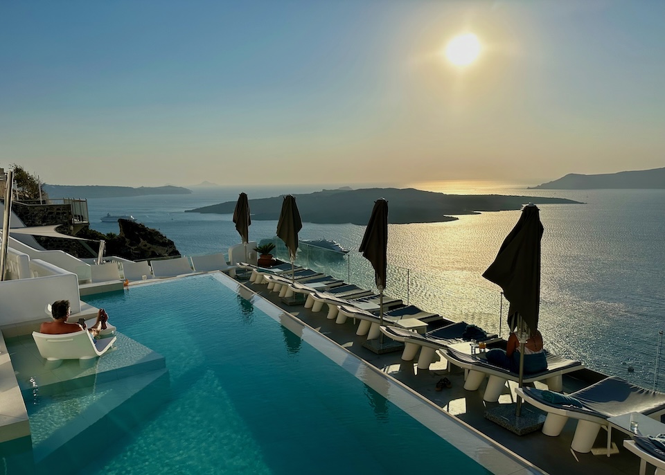 A man in a sunbed watches the sunset over the caldera and volcano, as seen from the infinity pool of Athina Luxury Suites in Fira, Santorini