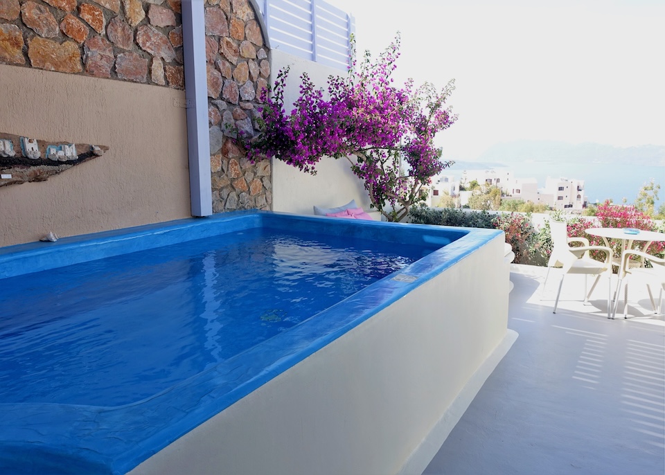 A blue-painted private plunge pool on a covered terrace behind a bougainvillea with views to the sea at Black Diamond suites in Akrotiri, Santorini.