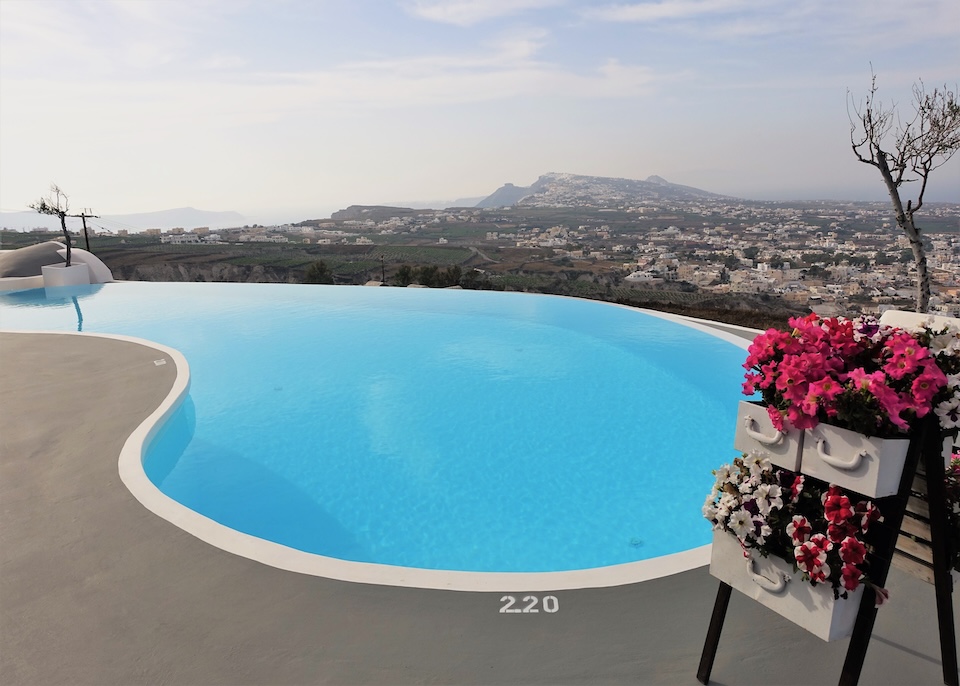 Baskets of flowers sit next to a kidney-shaped infinity pool with a panoramic view over Santorini at Carpe Diem hotel in Pyrgos village.