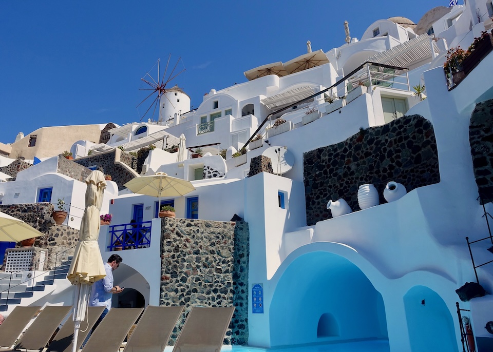 Facing in toward the cave-style pool and multi-level architecture of Esperas Hotel below a windmill in Oia, Santorini.