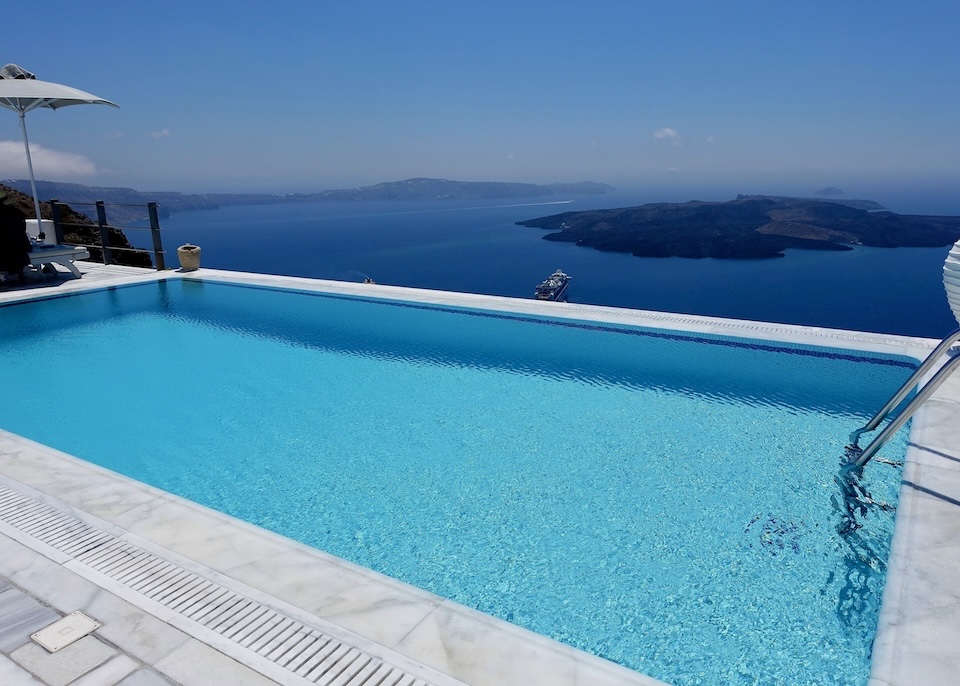 A crystal blue infinity pool overlooks the caldera and volcano at Homeric Poems hotel in Firostefani, Santorini.