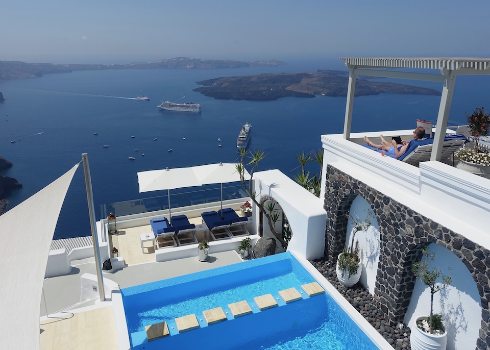 View from above a pool and sun terrace facing the caldera, volcanoes, and ferry boats at Iconic Hotel in Imerovigli, Santorini.