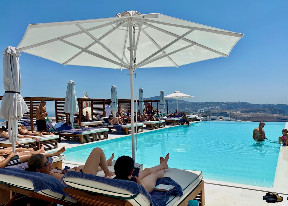 Couples and families enjoy the rooftop infinity pool and sunbeds at Katikies Garden hotel in Fira, Santorini.