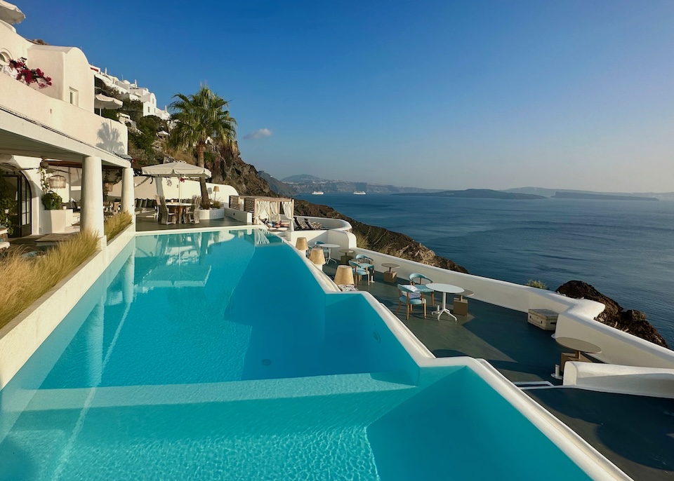 Long view of an infinity pool between two tiers of dining terraces overlooking the caldera at Katikies Kirini hotel in Oia, Santorini