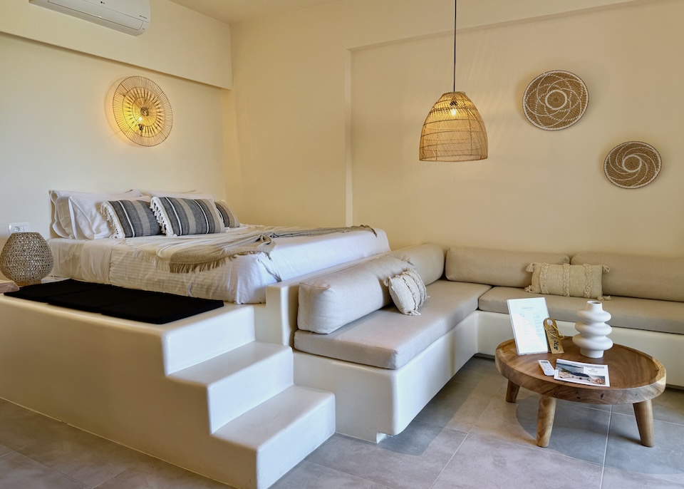 A boho chic room with a built in L-shaped sofa and elevated bed at Maeva Suites in Santorini.