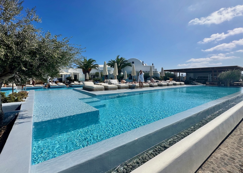 Wide-angle view of an infinity pool with an island of sunbeds in the middle at Nobu hotel in Imerovigli, Santorini.