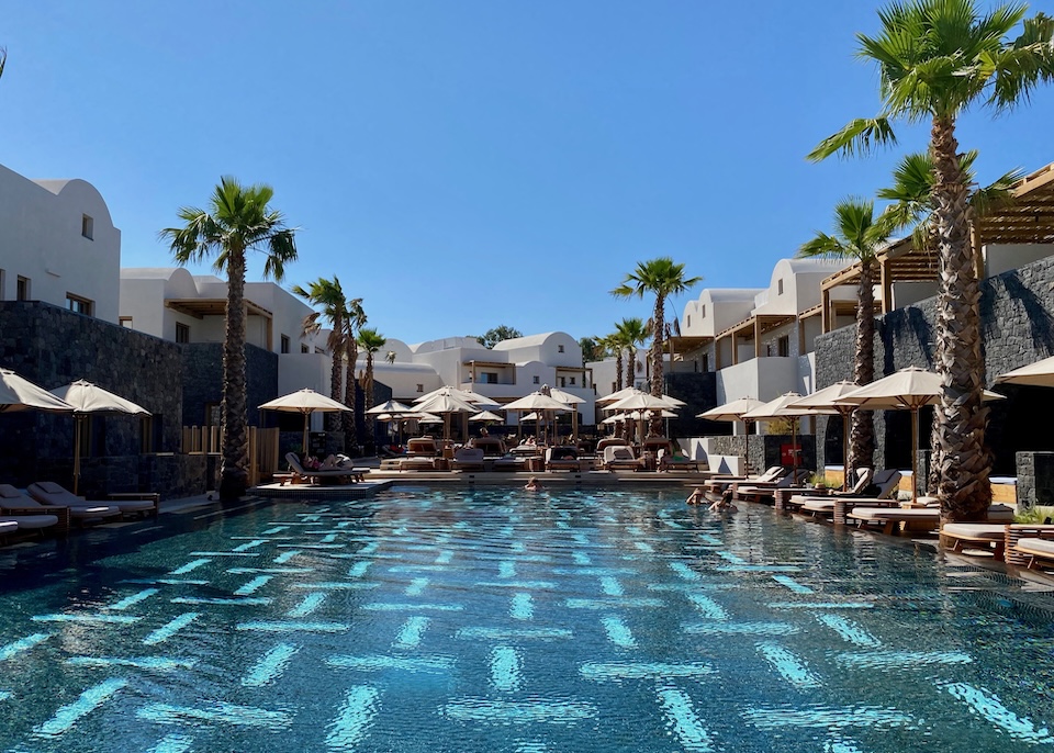 A large pool is ringed by sunbeds and palm trees at Radisson Blu Zaffron resort in Kamari, Santorini.
