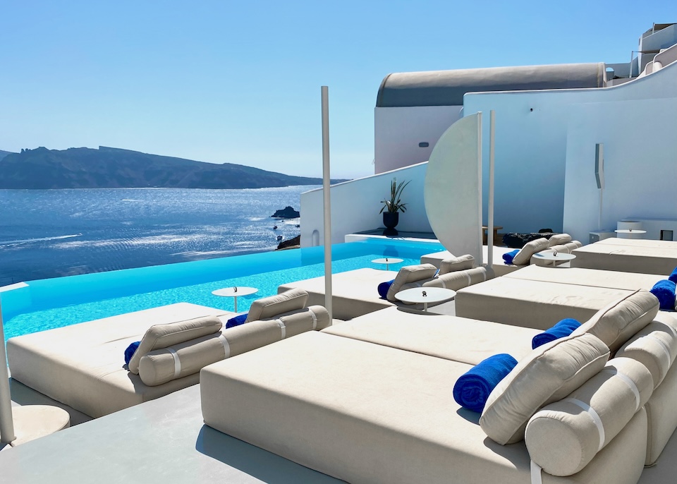 Two rows of double-sized sunbeds behind an infnity pool overlookign the caldera at Saint hotel in Oia, Santorini.