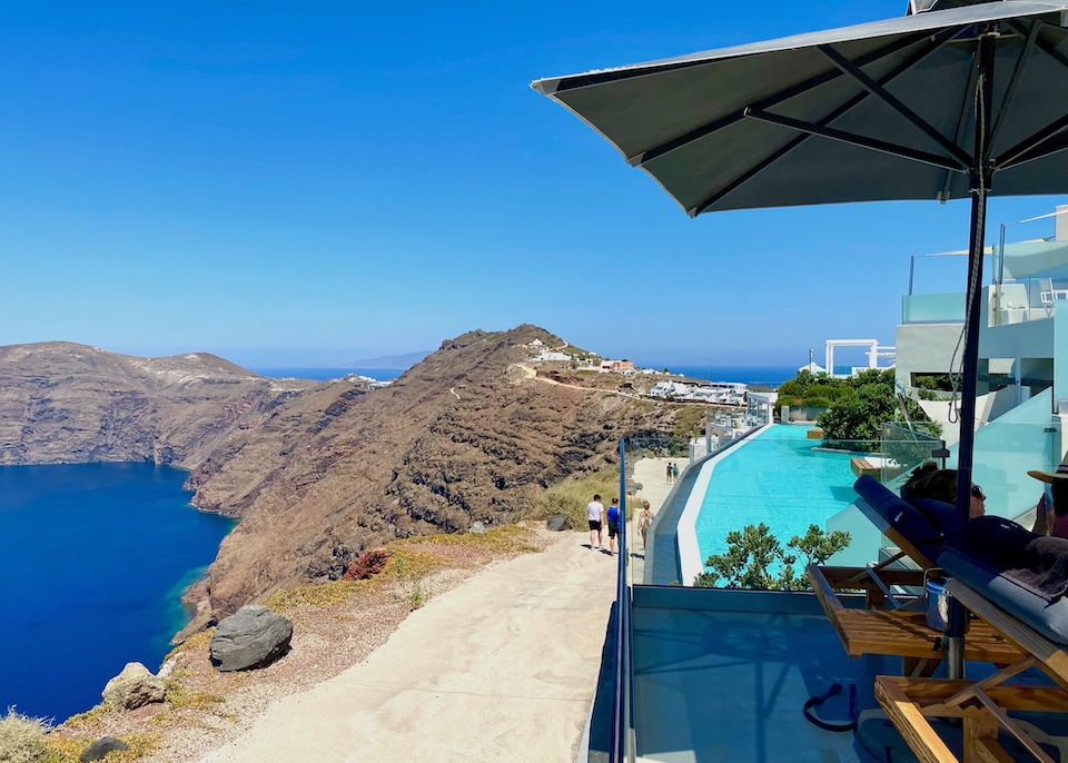 A shaded terrace and infinity pool overlook the Fira to Oia trail and the caldera at West East Suites in Imerovigli, Santorini.