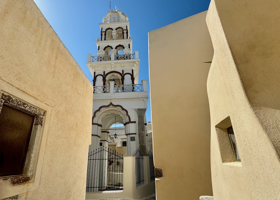 A narrow footpath leads to an elaborate bell tower with four tiers of bells and arabesque arches in Emporio, Santorini.