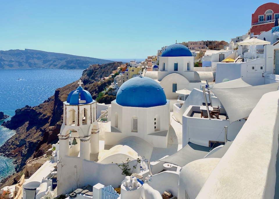 The iconic blue domed churches in Oia, Santorini with a bell tower and caldera below
