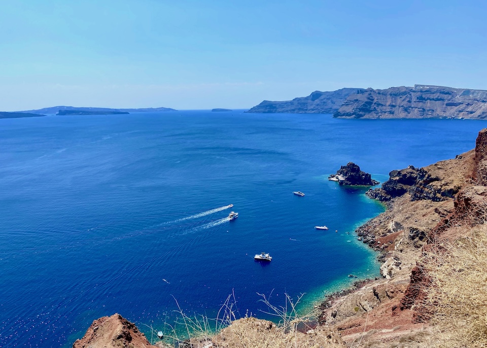A blue expanse of sea in the caldera facing Thirassia Island and the volcanoes, overlooking a few small boats in Santorini.