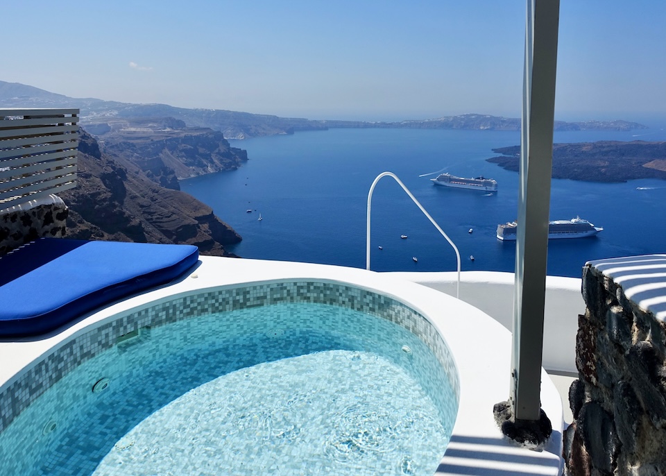 An oval-shaped tile jacuzzi above the caldera with a view of the volcanoes and cruise ships at Iconic hotel in Imerovigli, Santorini.